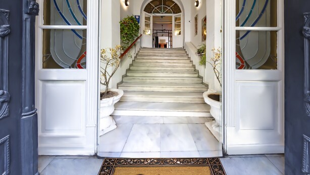 A grand entrance with a staircase leading to a second-floor landing, a welcome mat, and a decorative glass door with a geometric pattern. - Cezayir Rooms (Istanbul)