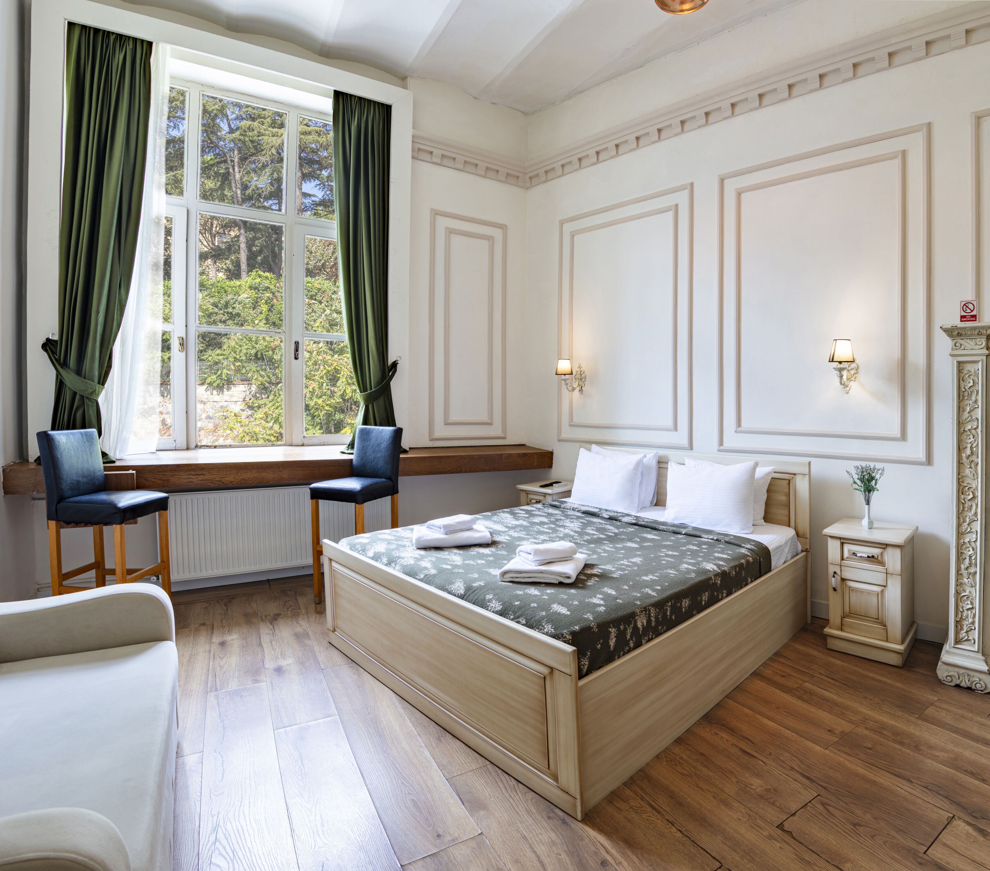 A bedroom with a large bed, two chairs, a nightstand, and a window with curtains.