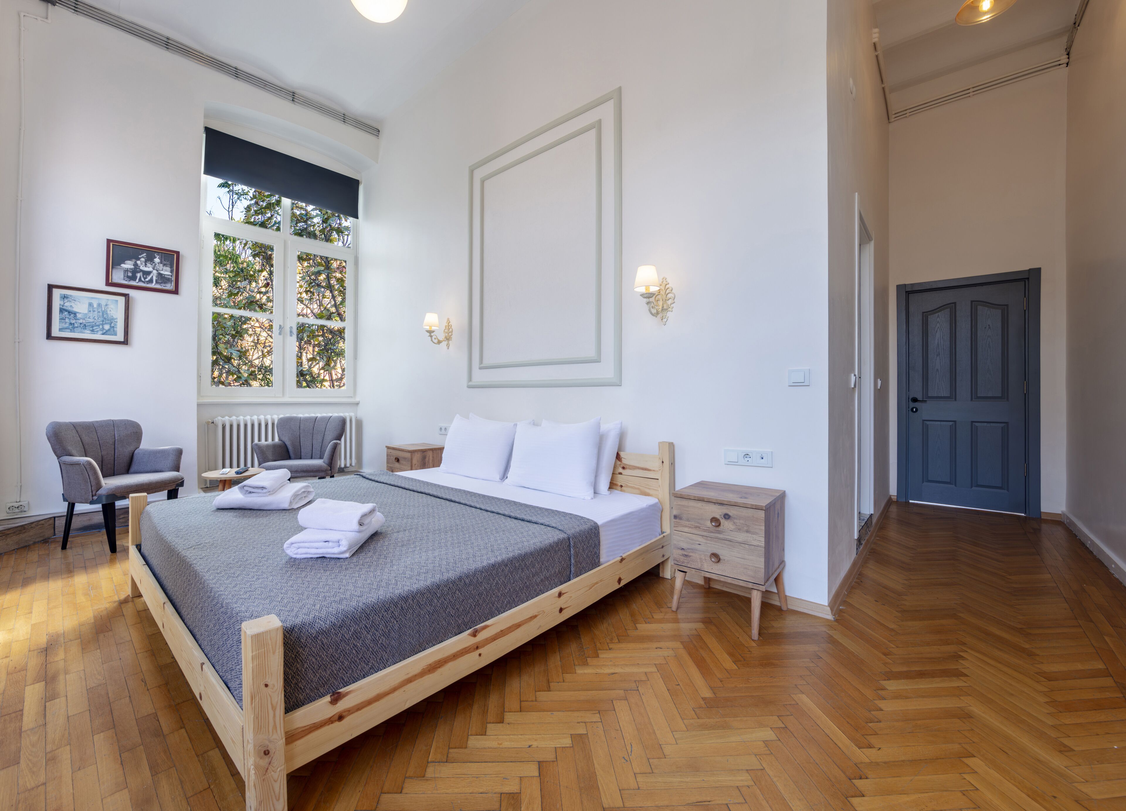 A bedroom with a wooden bed, a chair, a nightstand, and a window with a view of trees.