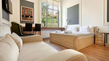 A modern hotel room with a large bed, a sofa, a desk, and a window with blinds.