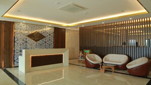 Ein Hotel-Empfangsbereich im modernen Stil, mit einer Rezeption, zwei Ledersesseln und einer Wand mit geometrischen Mustern.