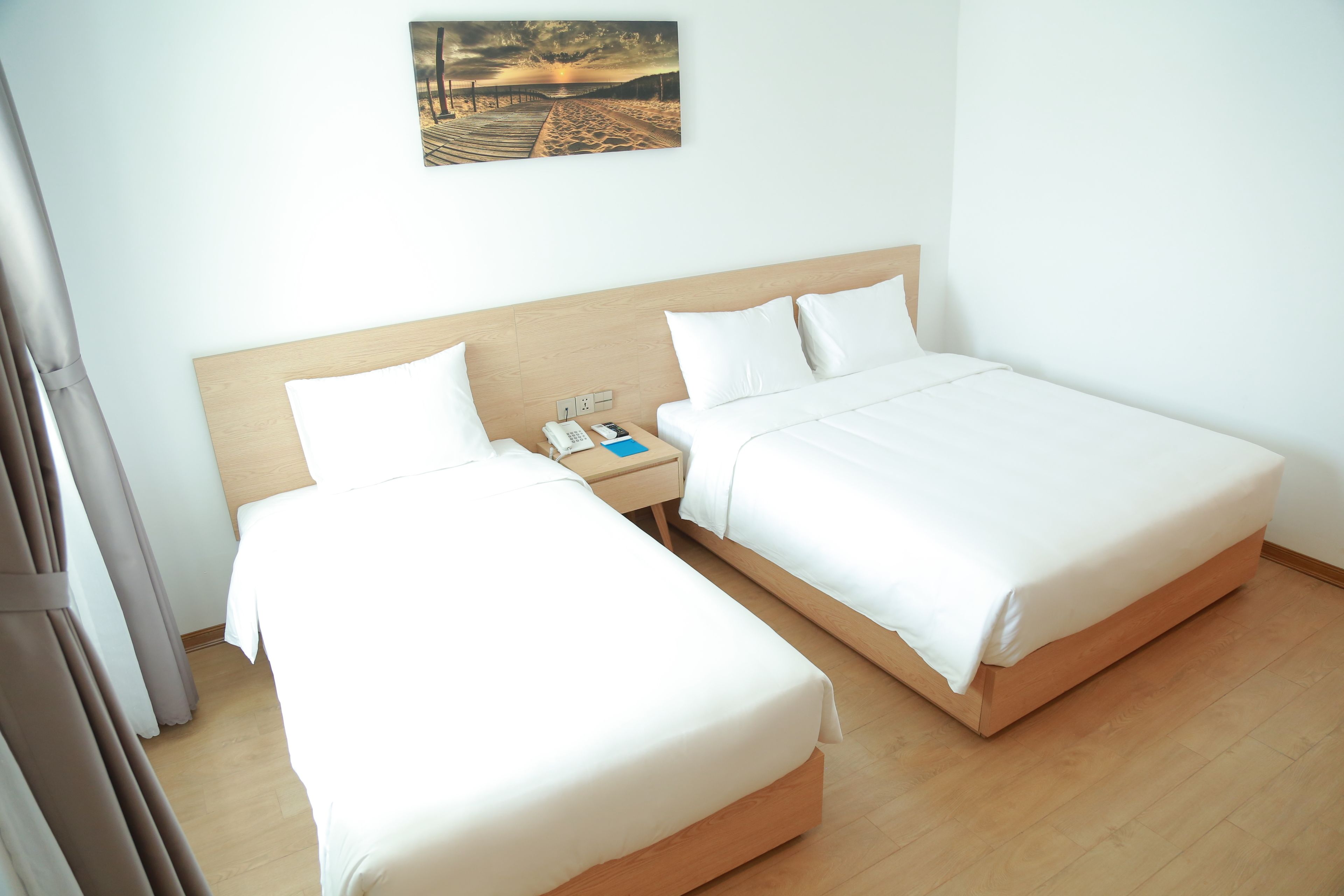 A hotel room with two beds, a wooden headboard, a nightstand with a phone and a book, and a painting on the wall.