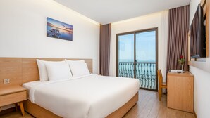 Ein modernes Hotelzimmer mit einem großen Bett, einem Holztisch, einem Flachbildfernseher und einem Balkon mit Meerblick.