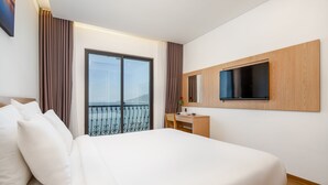 Ein Hotelzimmer mit einem großen Bett, einem Schreibtisch, einem an der Wand befestigten Fernseher und einem Balkon mit Aussicht.