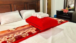 A neatly made bed with white linens, a red pillow, and a floral-patterned bedspread. - Family Ties GUEST INN (Bandarawela)