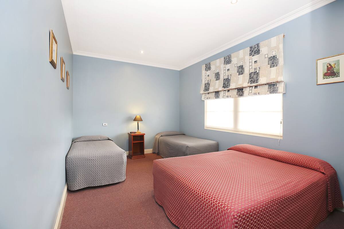A bedroom with two single beds, a small table with a lamp, and a window with a patterned valance.