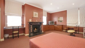 A room with a fireplace, a television, a dining table with chairs, and a bed with a patterned bedspread. - Grand Central Accommodation B&B Cobden (Cobden)
