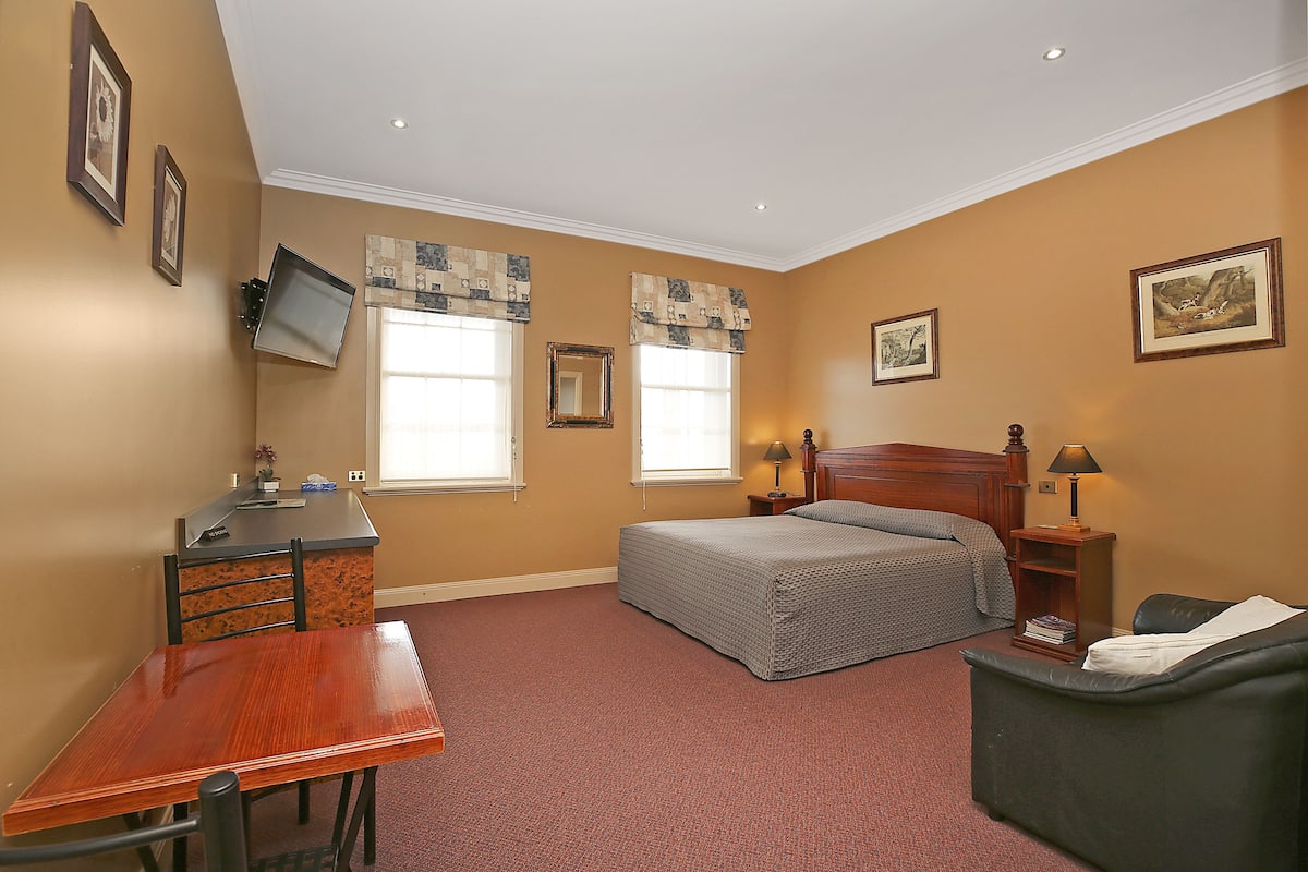 A bedroom with a bed, a desk, a chair, a nightstand, and a lamp.