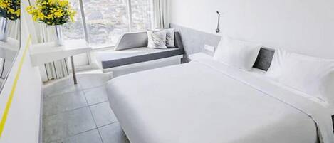 Habitación de hotel moderna con una cama grande, un escritorio pequeño y vistas de la ciudad a través de amplios ventanales.