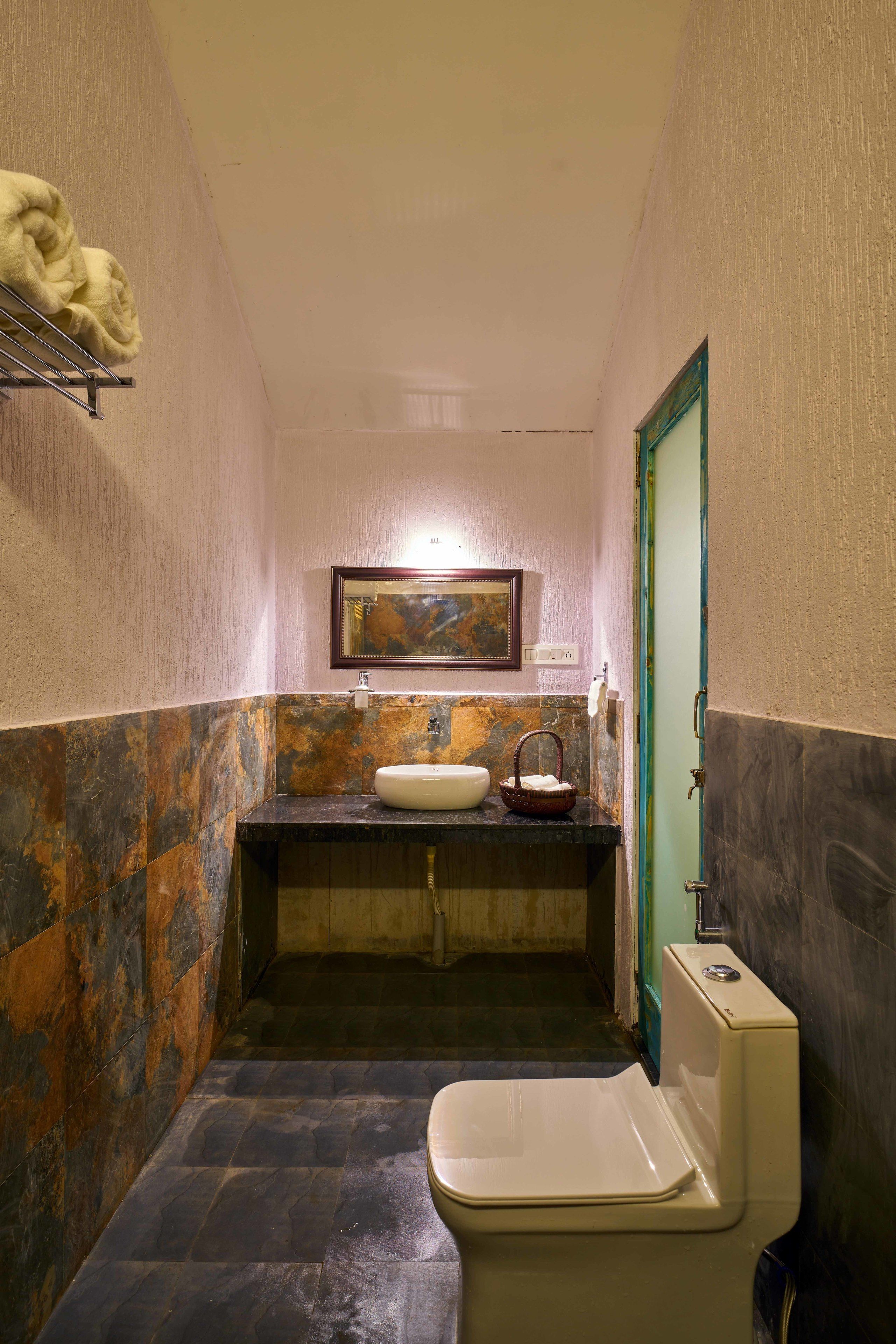 Un baño estrecho con inodoro blanco, lavamanos con encimera de mármol y un cuadro en la pared.