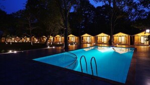 A nighttime swimming pool with a clear water surface, surrounded by trees and illuminated buildings. - Blu Resorts (Vagator)