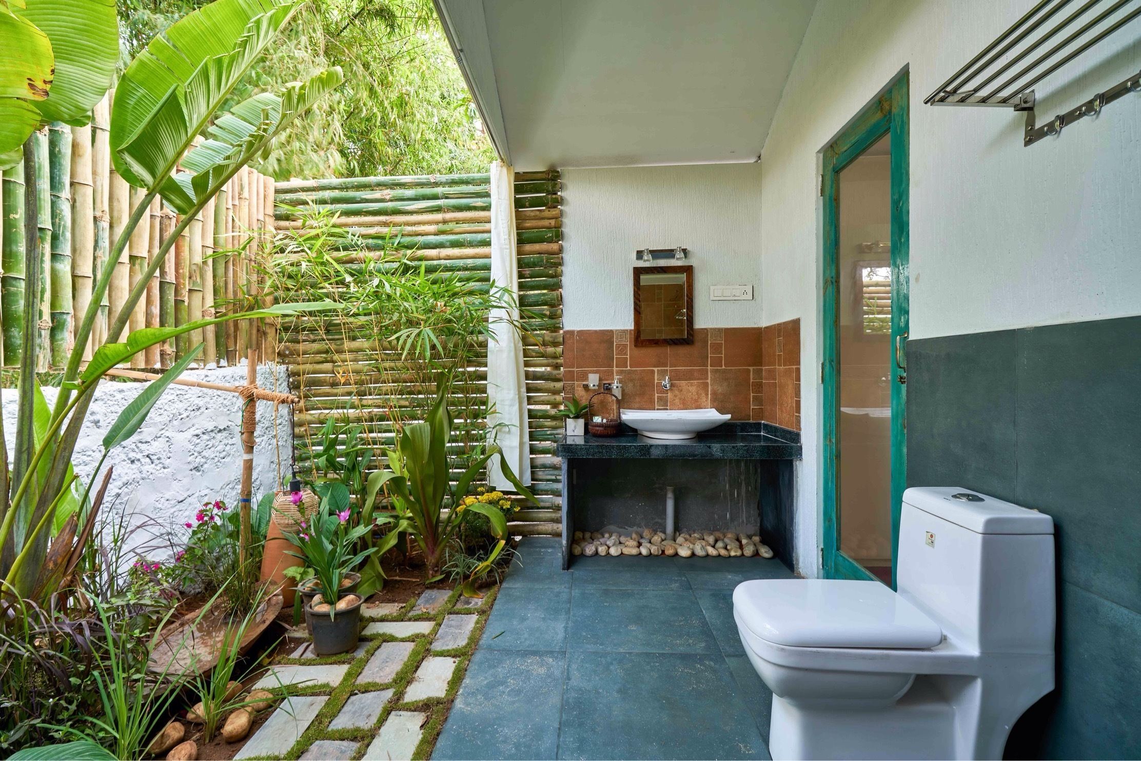 Een badkamer met een wit toilet, een wastafel en een spiegel. Een bamboescherm en diverse planten omringen de ruimte.