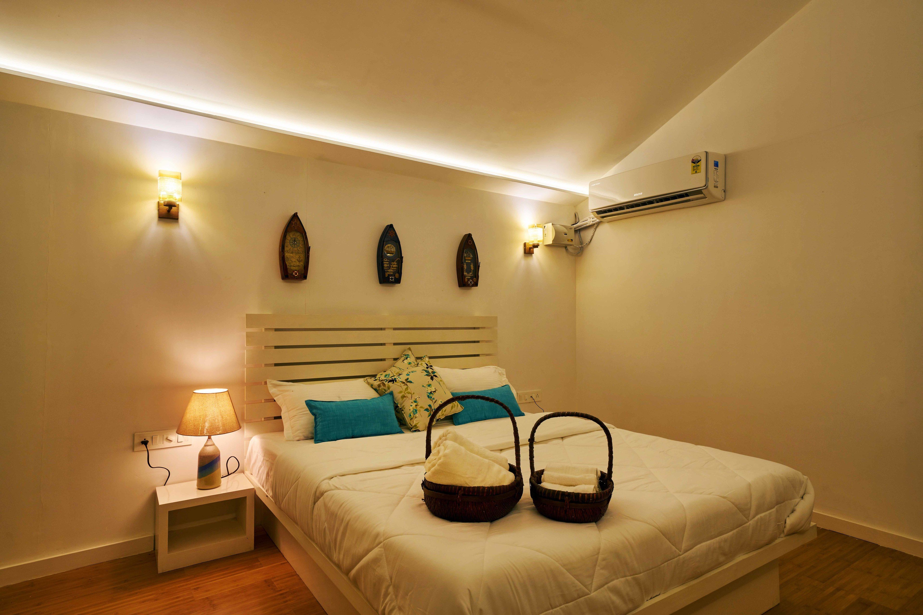 A neatly arranged bedroom with a bed, bedside lamp, wall-mounted air conditioner, and decorative wall sconces.