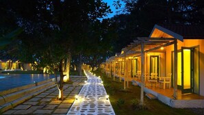 A pathway leading to a building with outdoor seating and a pool. - Blu Resorts (Vagator)