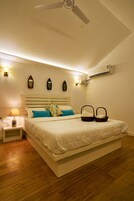 Un dormitorio con cama, mesita de noche, lámpara, aire acondicionado de pared y ventilador de techo.