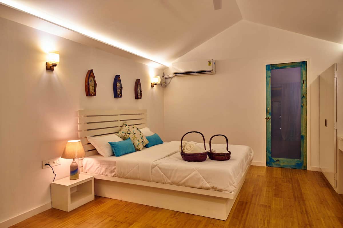 A bedroom with a bed, bedside lamp, wall-mounted air conditioner, and a door with a curtain.