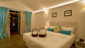 A neatly made bed with two baskets, a nightstand with a phone, and a door leading to a hallway with a mirror and a coat rack. - Blu Resorts (Vagator)