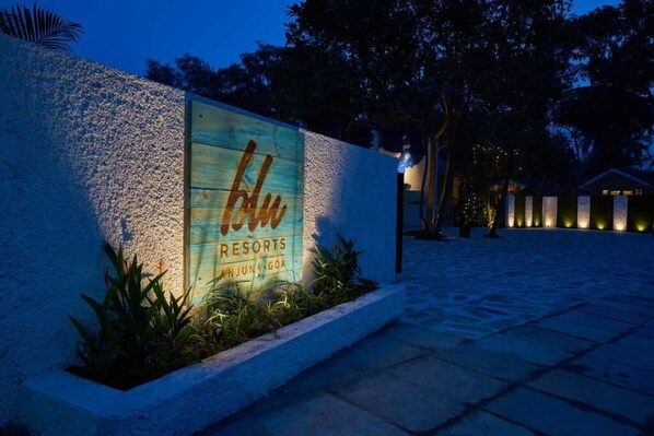 A sign for 'Blue Resorts' with a rustic wooden design, located in a paved area with a stone wall and some greenery.