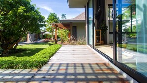 Una casa moderna con terraza de madera, puerta de vidrio y un jardín cuidado con palmeras.