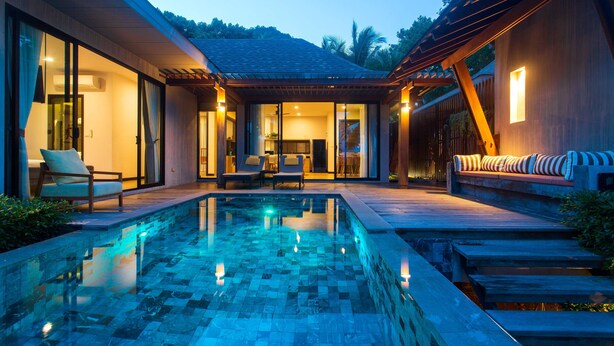 Un área de piscina moderna al aire libre con suelo de baldosas, rodeada de una terraza de madera y mobiliario de descanso.