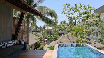 A pool area with wooden deck and lounge seating, surrounded by palm trees and a view of other buildings.