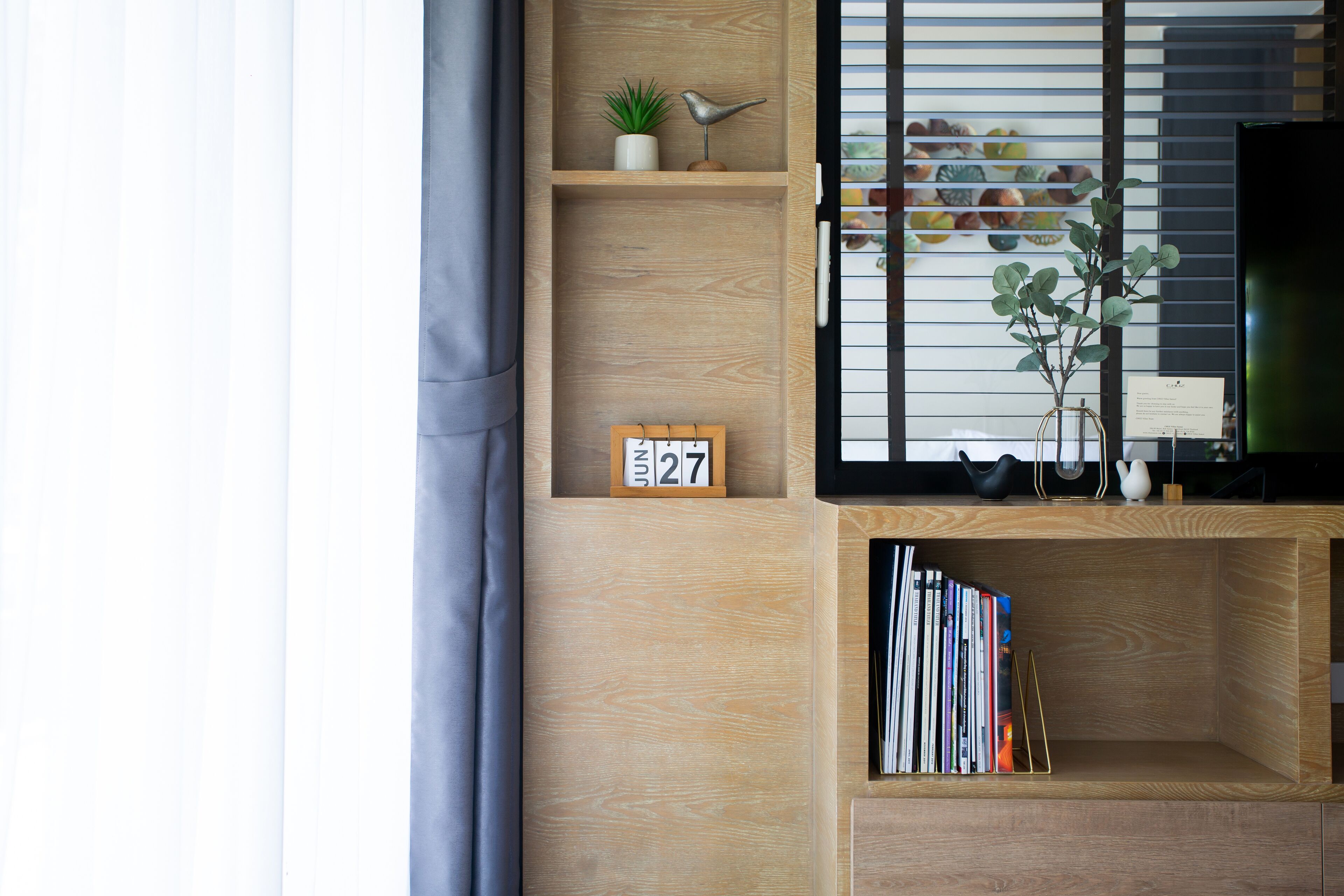 Een houten plank met een klein plantje, een ornament in de vorm van een vogel en een kalender waarop 27 juni staat.