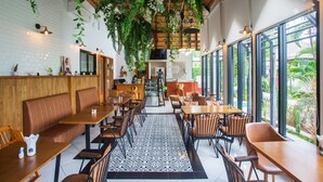 Un restaurante con mesas y bancos de madera, un tapiz a cuadros blanco y negro y plantas colgantes.