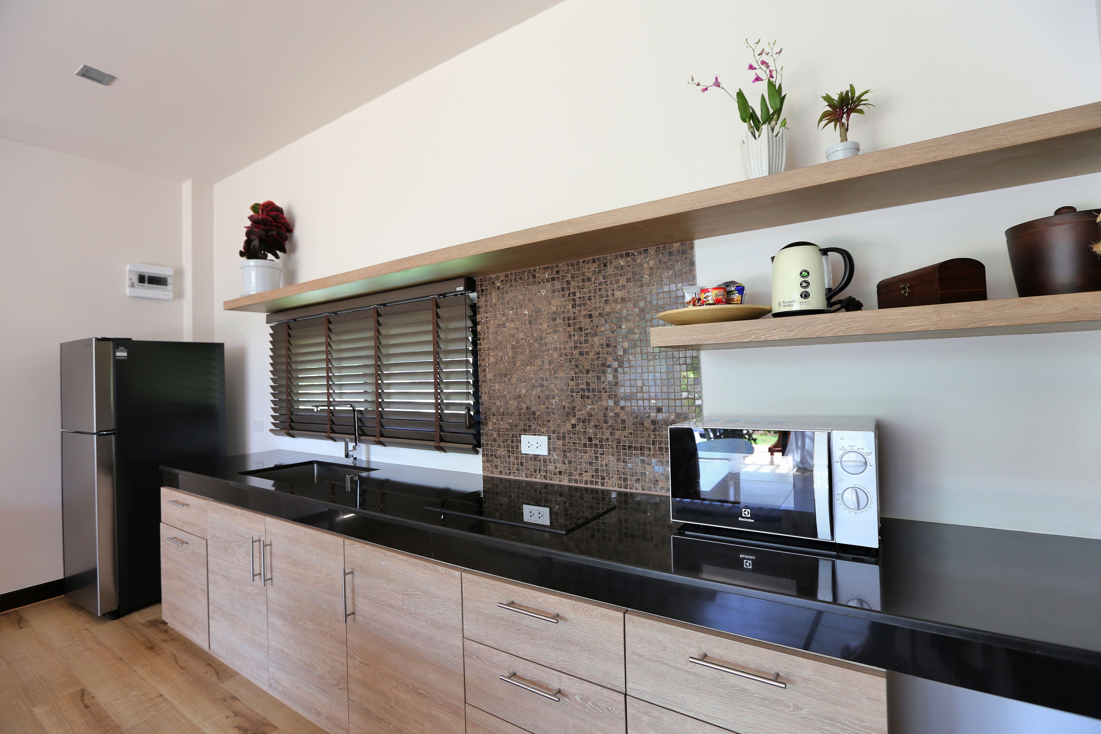 A modern kitchen with a black countertop, wooden cabinets, and a backsplash.