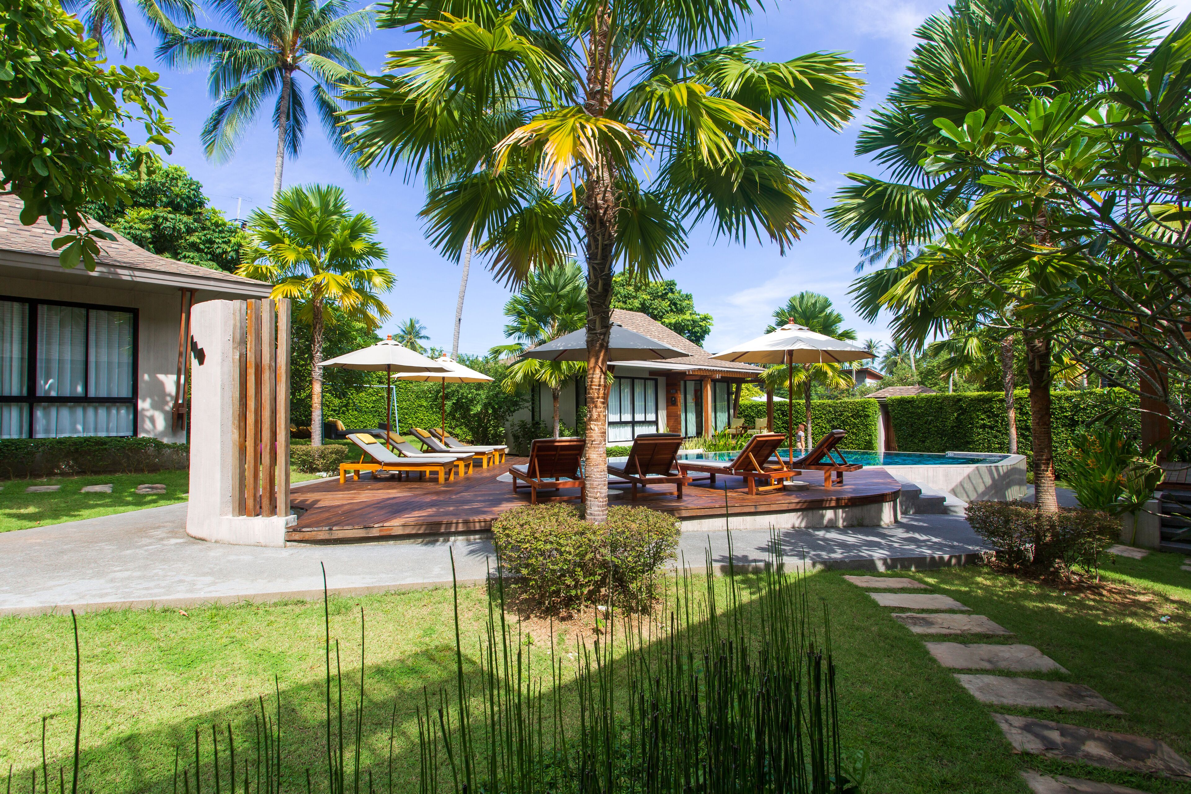 A resort with a pool, lounge chairs, palm trees, and a well-maintained lawn.