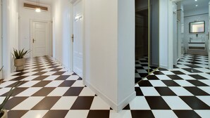 Un couloir avec un sol à carreaux noirs et blancs, des murs blancs et une porte au fond.