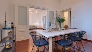 Un coin repas avec une table blanche, des chaises en fil de fer noir et un vase rempli de fleurs.