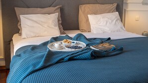 Un lit bien fait, recouvert d’une couverture à carreaux bleus, avec deux oreillers, un plateau sur lequel se trouvent un bol de myrtilles, une tasse et un livre.