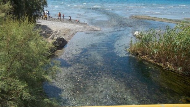 Une rivière aux eaux claires, bordée d’un rivage rocheux, où l’on peut voir des gens se promener.