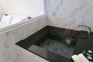 A modern bathroom with a black bathtub, a window with white curtains, and a marble wall. - Instay (Puli)