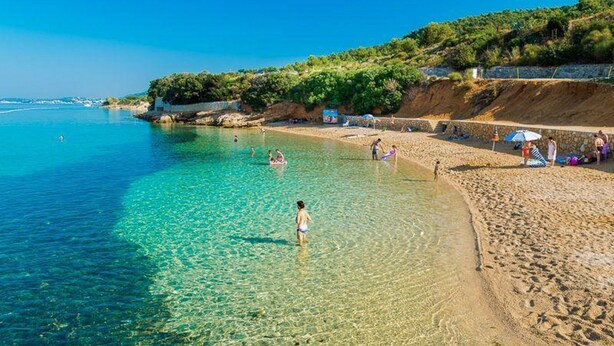 A beach with clear water, people swimming, and a sandy shore with umbrellas. - Holiday House Perkic mm (Rab)
