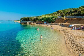 Una playa con agua cristalina, gente nadando y una orilla arenosa con sombrillas.
