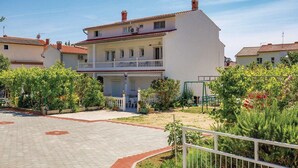 A two-story building with a balcony, surrounded by greenery and a paved courtyard. - Holiday House Perkic mm (Rab)