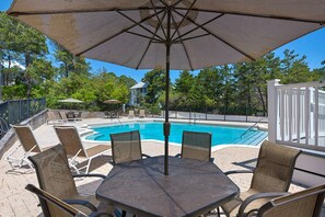 A poolside area with a table and chairs, a large umbrella, and a pool.