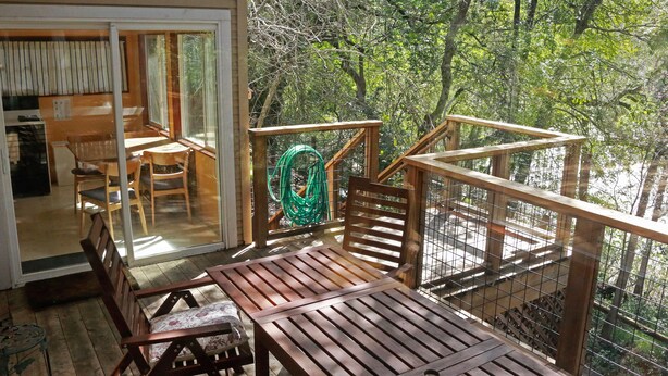 A wooden deck with a table and chairs, a green garden hose, and a view of trees.