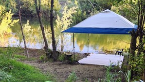 A tent with a blue canopy, a kayak, and a chair by a lake surrounded by trees.