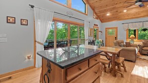 A spacious room with a large wooden ceiling, a dining area with a glass-top table, and a view of the outdoors. - Luxury Cabin | Hot Tub & Game Room Near Highlands (Franklin)