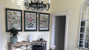 A dining area with a glass table surrounded by chairs, a chandelier, and framed botanical prints on the wall. - River Front Estate (Huonville)
