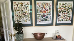 A room with a wooden table displaying botanical prints, a copper pot, and a vase with flowers. - River Front Estate (Huonville)