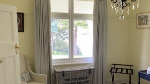 A room with a bed, a chair, a chest of drawers, a window with curtains, a chandelier, and a framed picture on the wall. - River Front Estate (Huonville)