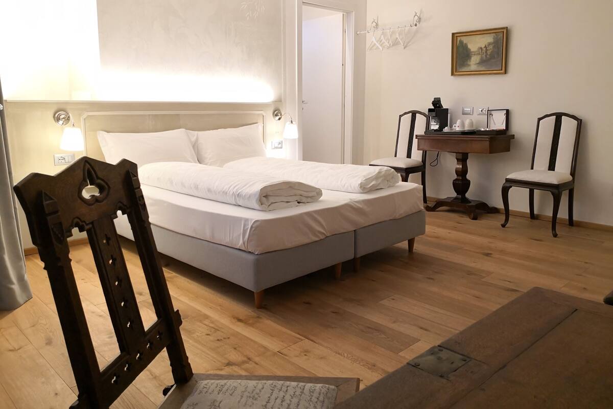 A bedroom with a bed, a chair, a desk, and a painting on the wall.