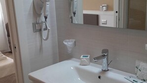 Un baño con lavamanos blanco, un espejo, un secador de pelo y un perchero para toallas.