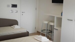 Un dormitorio con cama, televisor montado en la pared y un armario blanco.