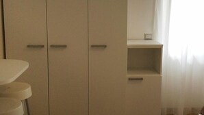 Habitación con un armario grande, un estante pequeño y una ventana con cortinas.