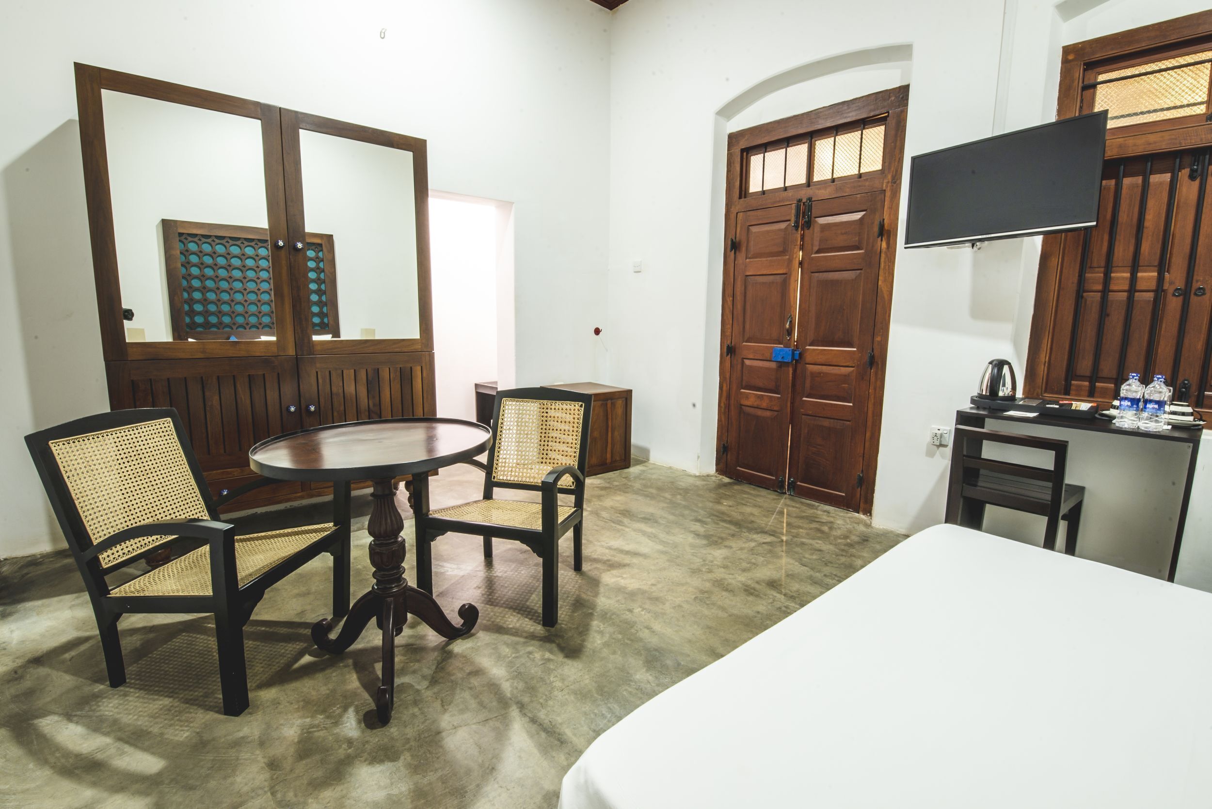 A room with a bed, two chairs, a round table, a television, and a wooden door.