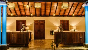 A hotel lobby with two wooden reception desks, a large wooden door, and a ceiling with exposed beams and hanging light fixtures. - Thambu Illam (Jaffna)